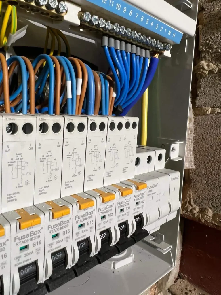 Electrical fuse box with labeled circuit breakers, colored wiring, and safety warnings about live terminals and fire risk