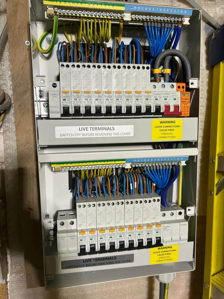 Electrical fuse box with labeled circuit breakers, colored wiring, and safety warnings about live terminals and fire risk