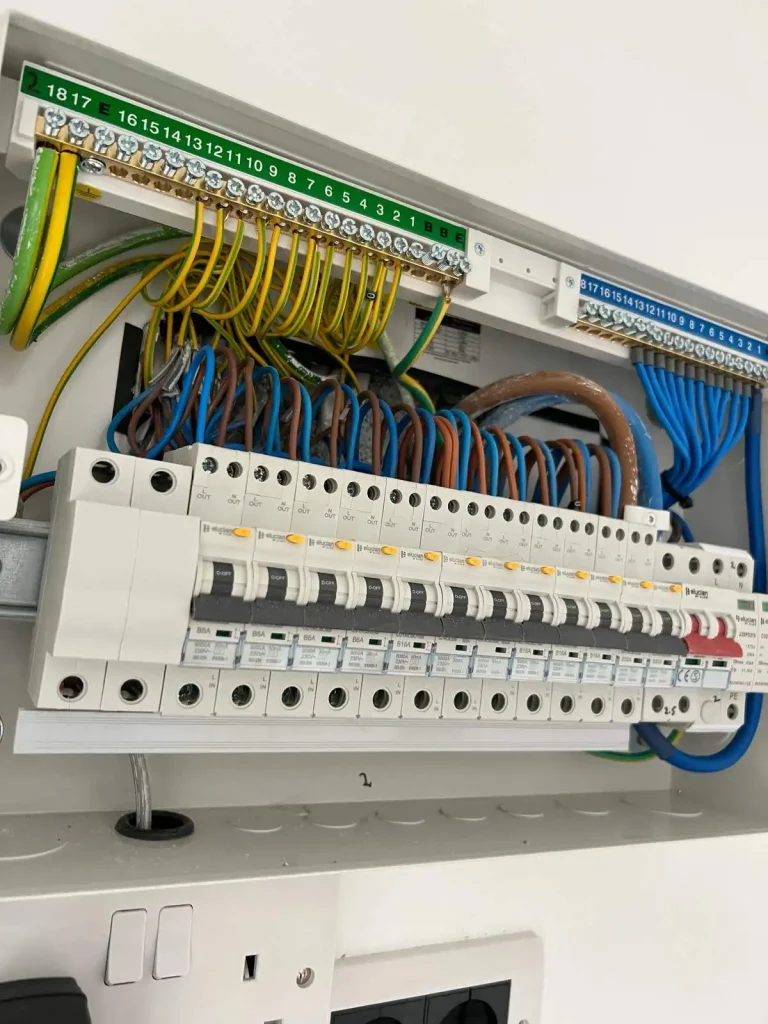 Electrical fuse box with labeled circuit breakers, colored wiring, and safety warnings about live terminals and fire risk