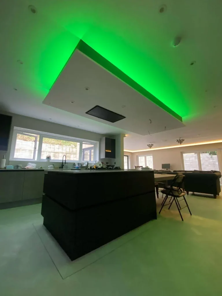 Modern open-plan kitchen and living area with central island, recessed ceiling featuring green LED lighting