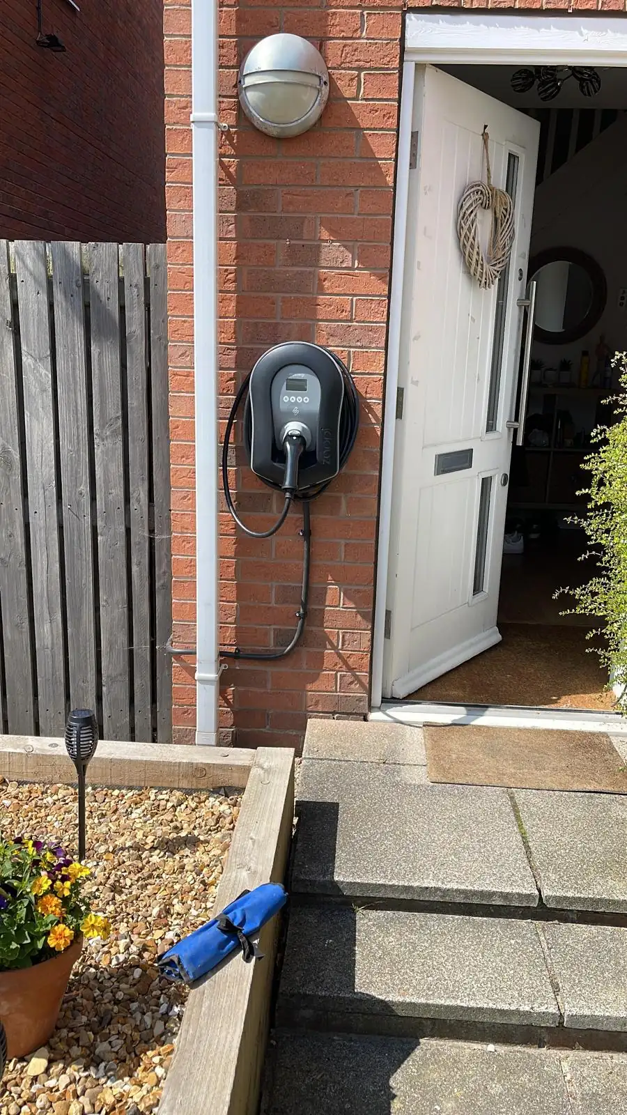 Wall-mounted EV charger with coiled cable installed beside open white door on brick house