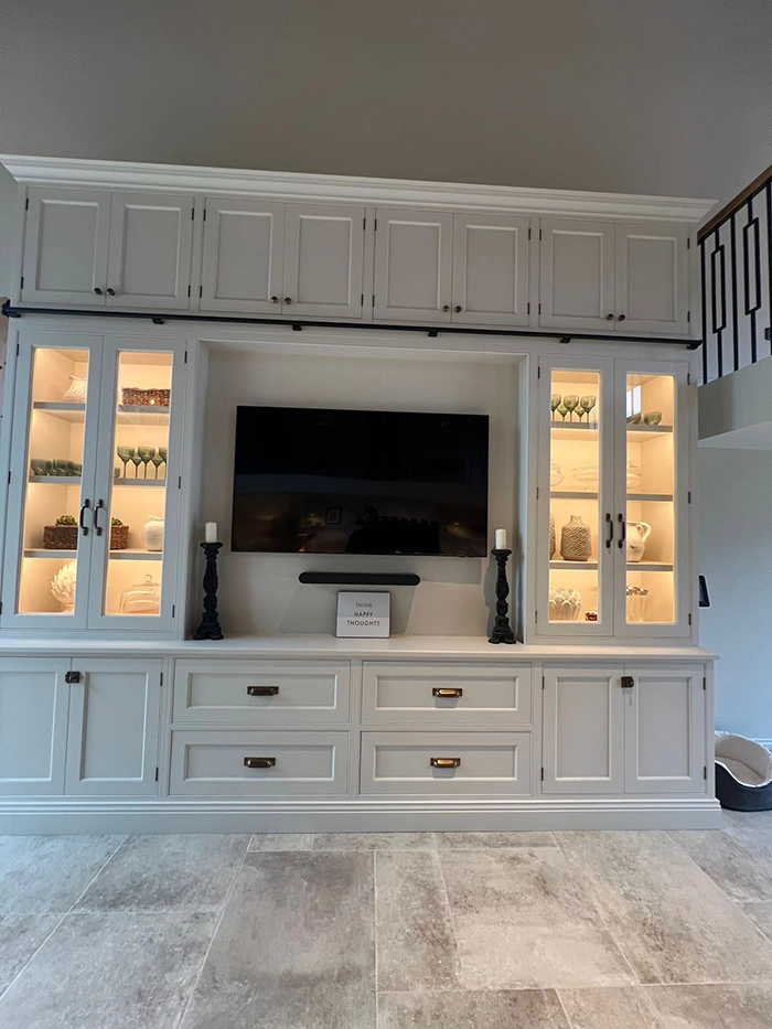 Built-in entertainment unit with large wall-mounted TV, glass-front cabinets displaying vases and ornaments that are highlighted with LED lights
